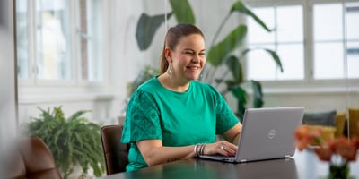 A woman is working at a desk on a computer and smiling at the screen.
