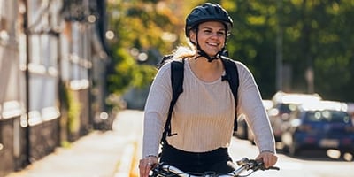 Hymyilevä nuori nainen polkee työsuhdepyörällä Helsingin katuja