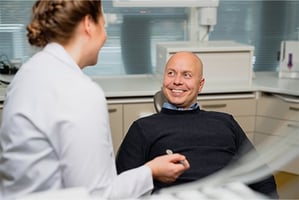 Hammaslääkäri, jolla on kädessä hammastarkastuspeili sekä mies, joka istuu hammaslääkärin tuolissa