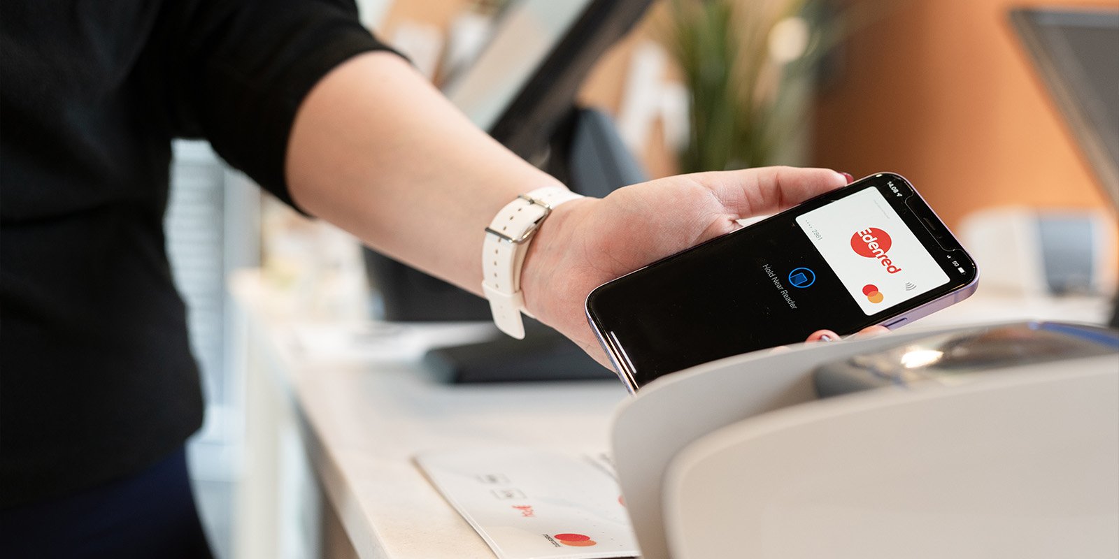  The phone that is in a person's hand next to the payment terminal. The screen shows Edenred's payment card in Apple Pay.