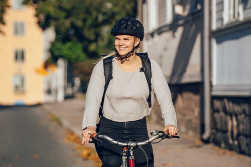 A young woman is cycling in the city. In the background, there are buildings and trees.
