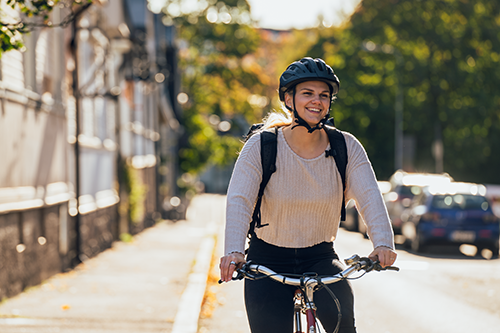 Hymyilevä nuori nainen polkee työsuhdepyörällä pitkin Helsingin katuja.